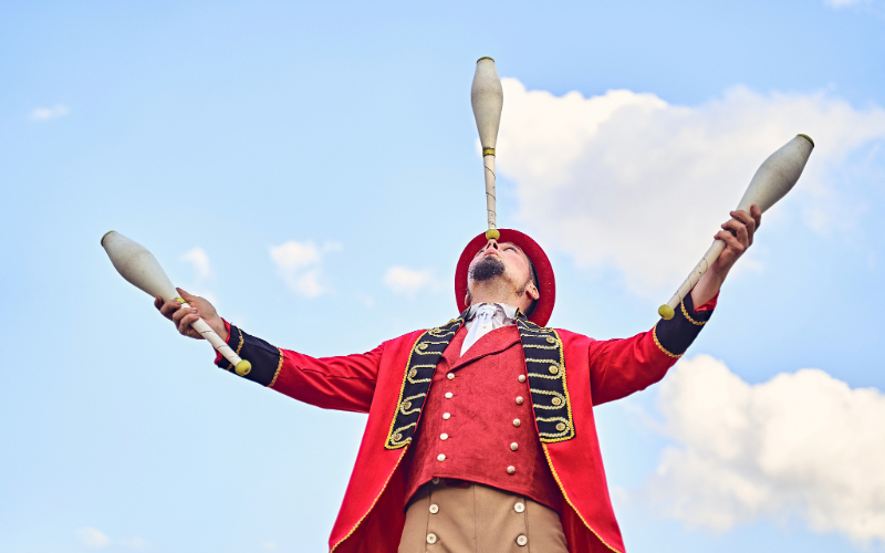 En cirkusartist jonglerar käglor under en blå himmel.